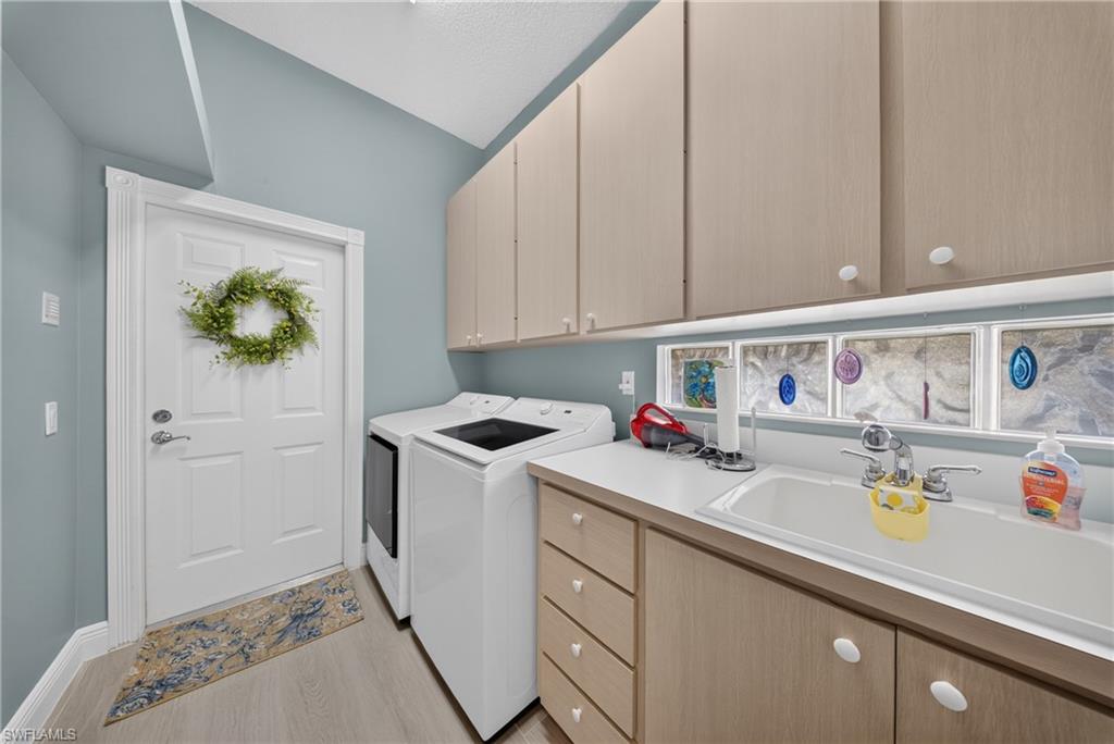 Functional utility space featuring light wood-finish cabinetry, a white countertop with an integrated sink, and light wood-finish flooring