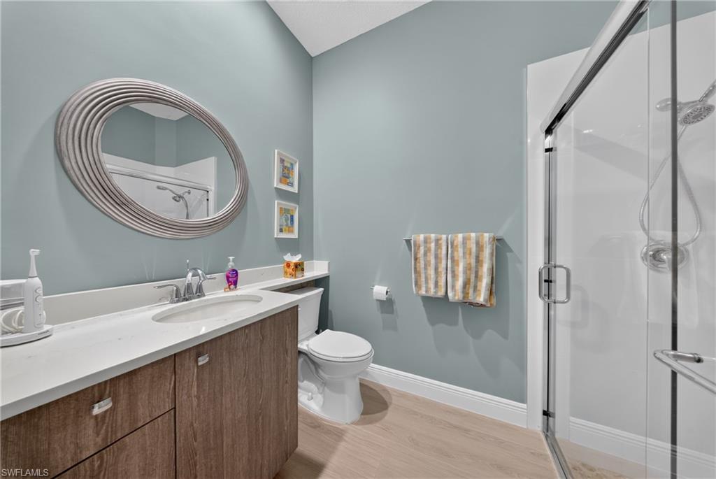 Bathroom featuring a wood-finish vanity with a single sink, light-toned countertop, and a contemporary oval mirror