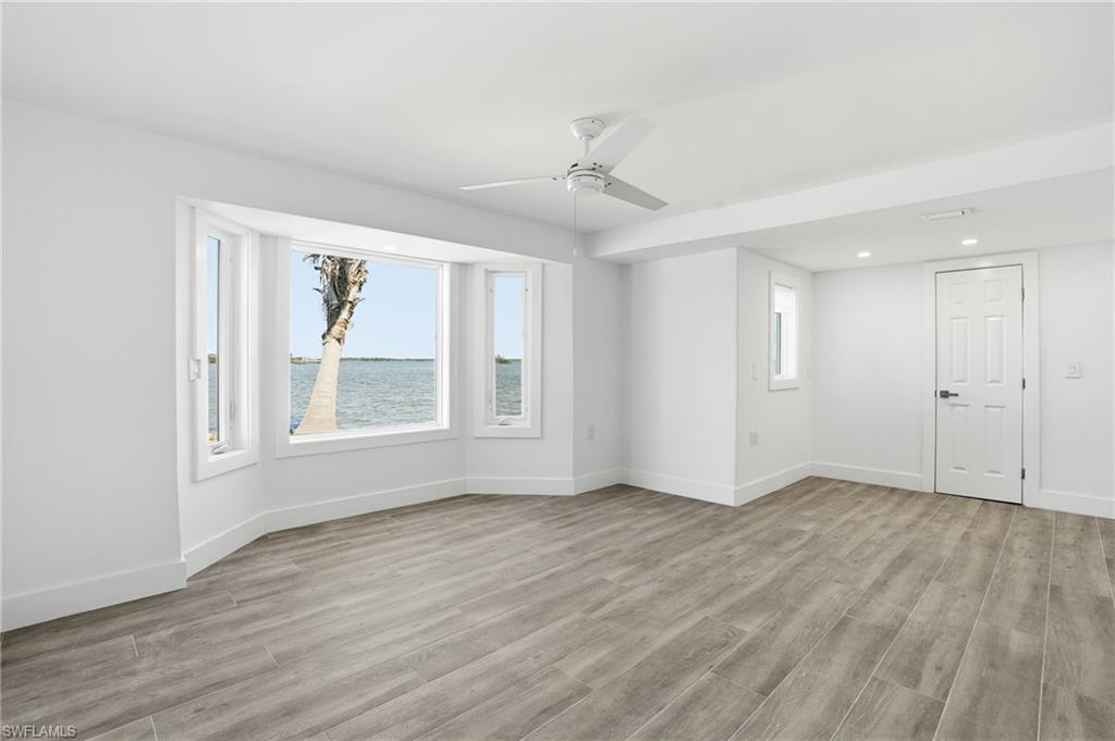 Empty room with light wood finished floors, ceiling fan, recessed lighting, and a water view - Virtually Edited Image