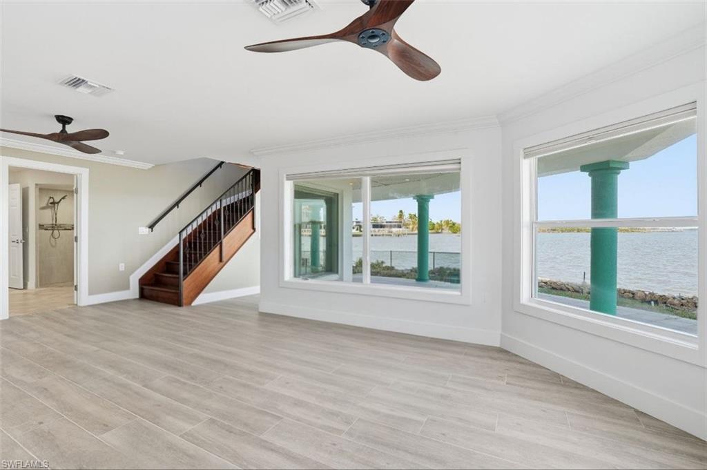 Unfurnished living room featuring ceiling fan, crown molding, stairs, light wood-style flooring, and a water view - Virtually Edited Image