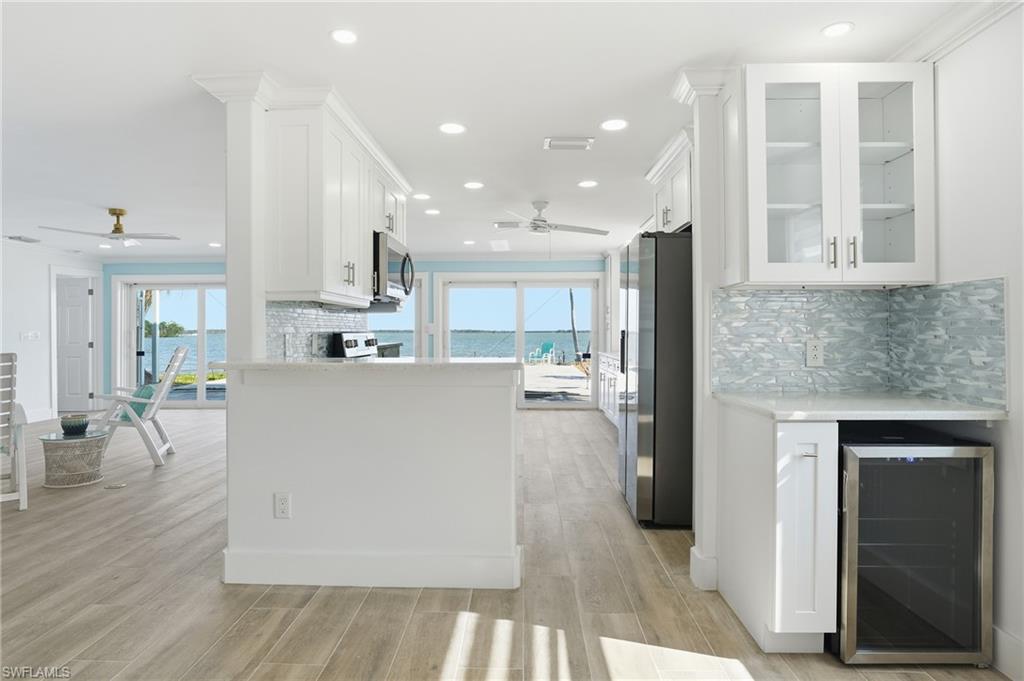 Kitchen with tasteful backsplash, white cabinets, wine cooler, and recessed lighting - Virtually Edited Image
