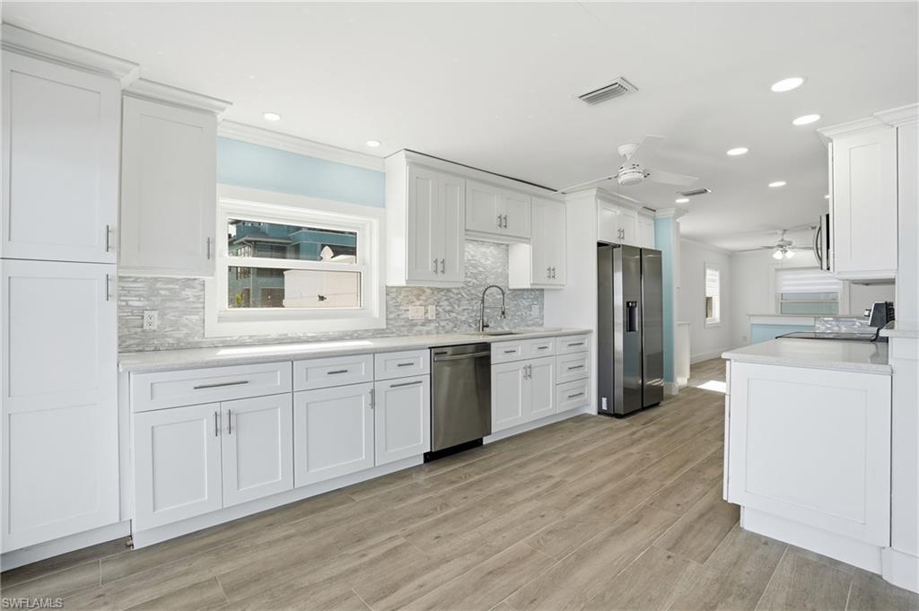 Kitchen with stainless steel appliances, a ceiling fan, white cabinetry, ornamental molding, and backsplash - Virtually Edited Image