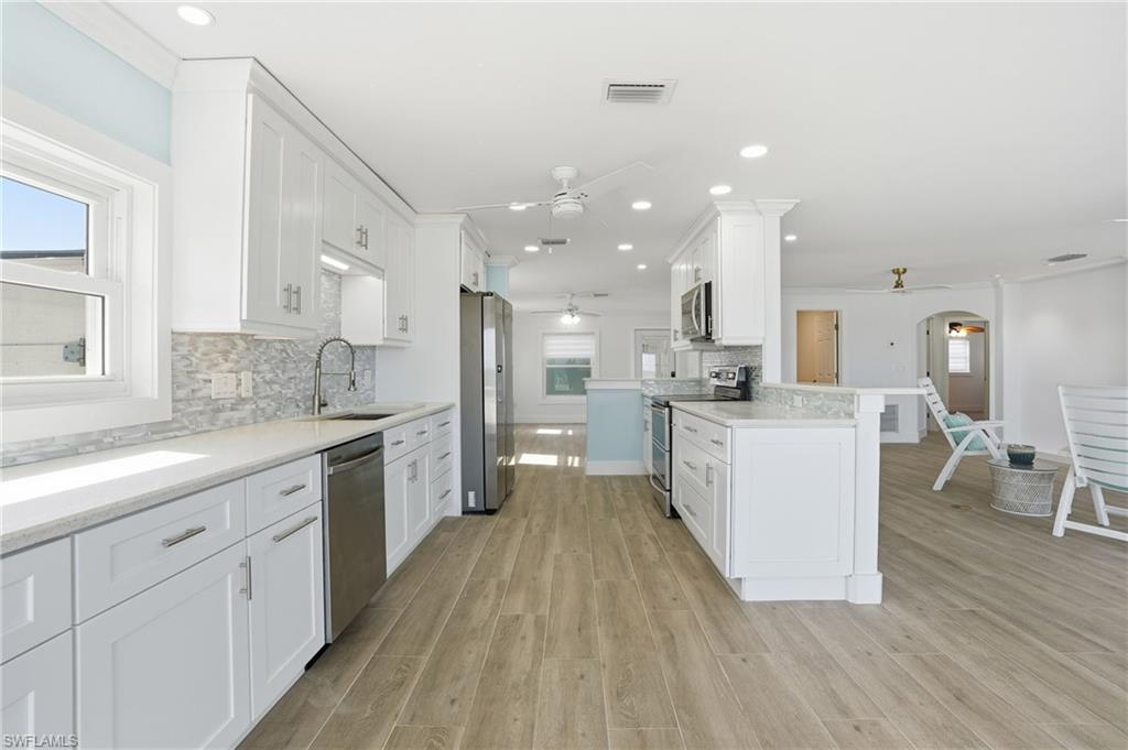 Kitchen with white cabinetry, backsplash, a ceiling fan, stainless steel appliances, and arched walkways - Virtually Edited Image