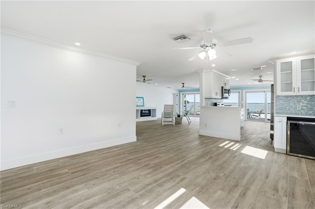 Living area with a fireplace, beverage cooler, recessed lighting, crown molding, and light wood finished floors - Virtually Edited Image