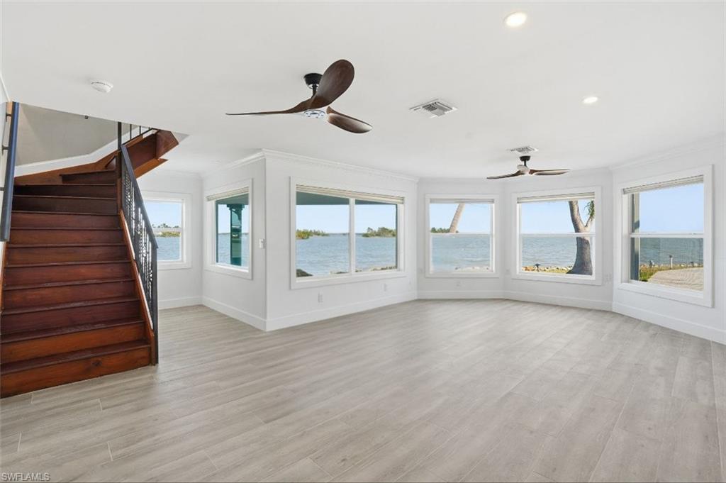 Unfurnished living room featuring a water view, stairway, light wood-style flooring, plenty of natural light, and ornamental molding - Virtually Edited Image