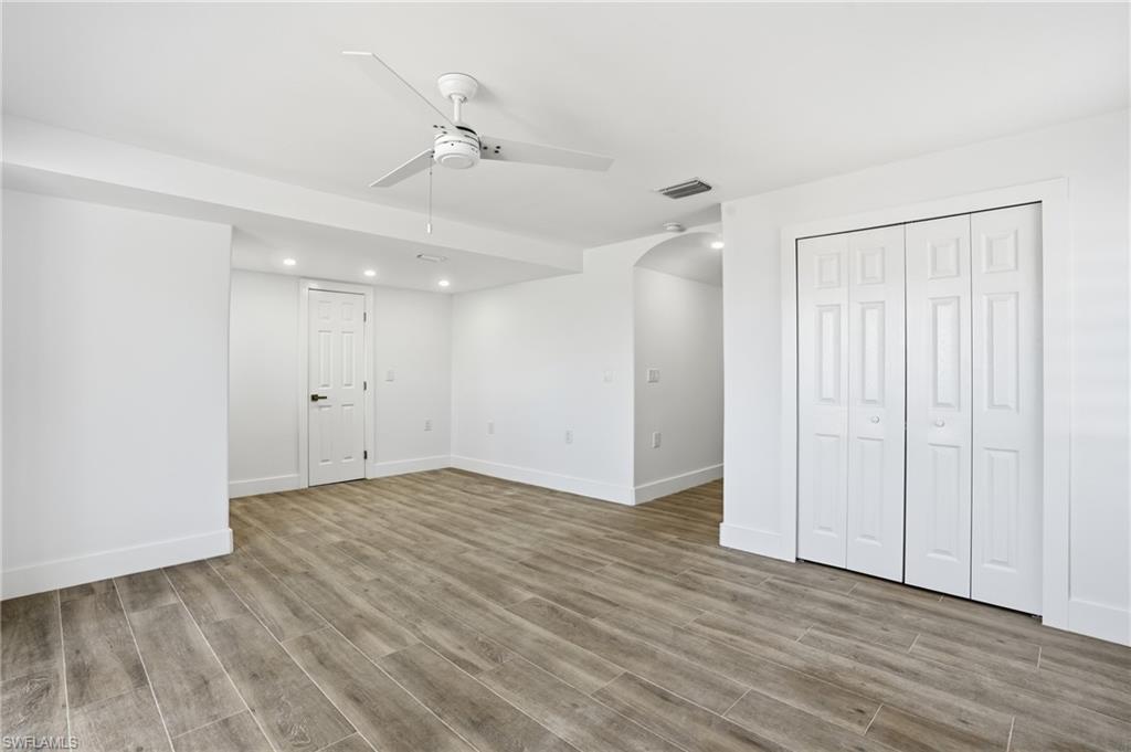 Unfurnished bedroom with arched walkways, light wood finished floors, recessed lighting, ceiling fan, and a closet - Virtually Edited Image