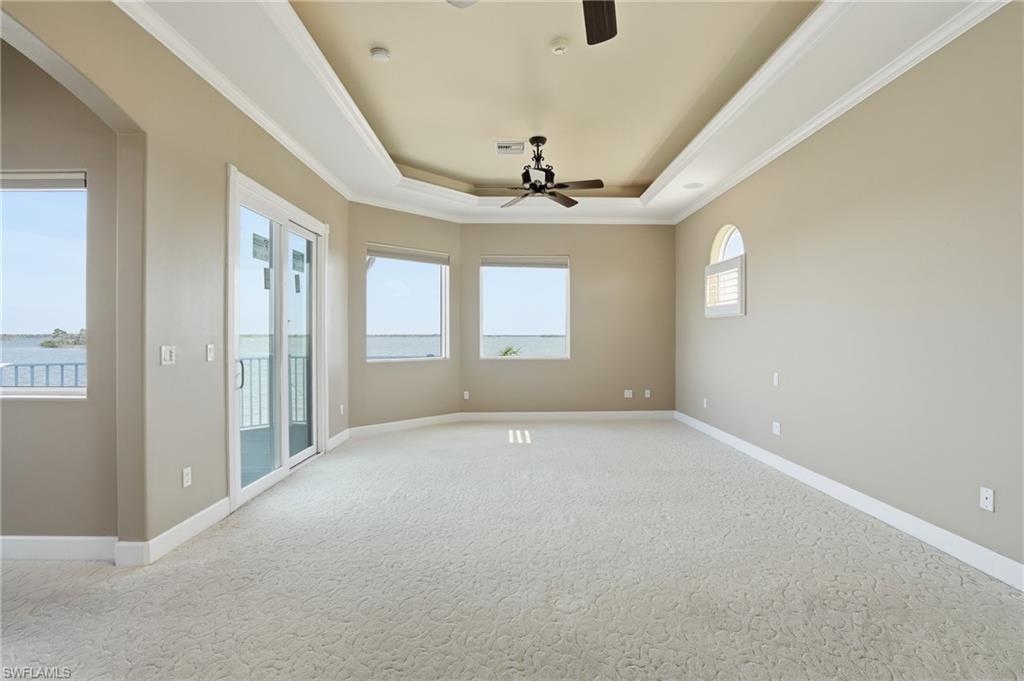 Empty room with arched walkways, crown molding, a tray ceiling, carpet, and a water view - Virtually Edited Image