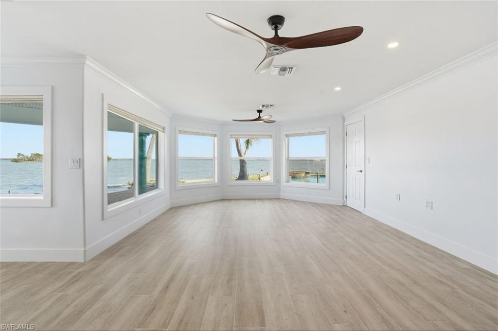 Unfurnished living room featuring ceiling fan, crown molding, light wood-style flooring, and a water view - Virtually Edited Image