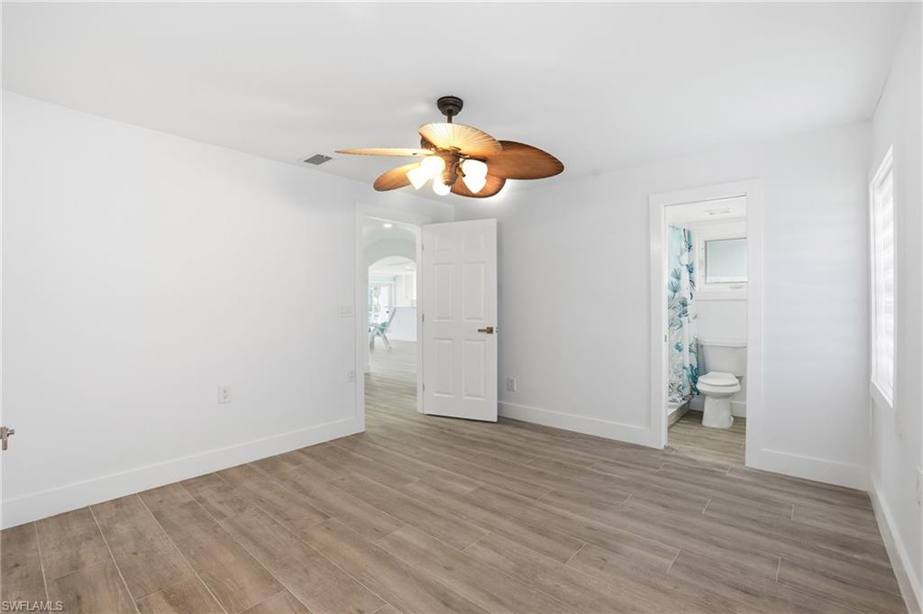 Unfurnished bedroom featuring wood tiled floors, ceiling fan, arched walkways, and ensuite bath - Virtually Edited Image