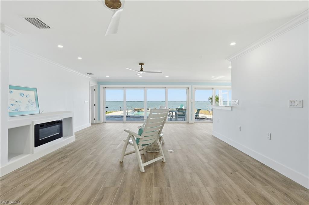 Living area featuring a water view, a glass covered fireplace, healthy amount of natural light, light wood-style floors, and ornamental molding - Virtually Edited Image