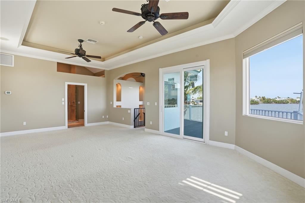 Empty room featuring a tray ceiling, crown molding, light colored carpet, and ceiling fan - Virtually Edited Image