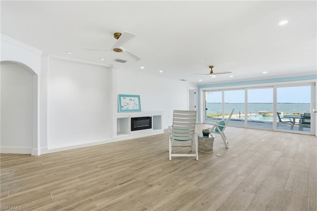 Living room featuring a water view, crown molding, a glass covered fireplace, light wood-style floors, and a ceiling fan - Virtually Edited Image