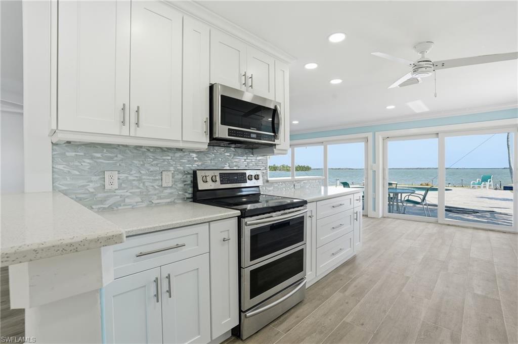 Kitchen with appliances with stainless steel finishes, crown molding, white cabinets, a water view, and recessed lighting - Virtually Edited Image