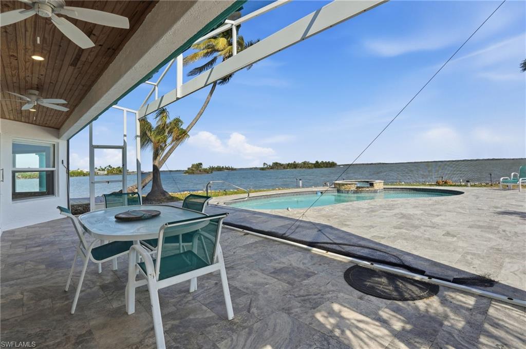 View of patio / terrace with ceiling fan, a water view, a lanai, a sunroom, and a pool with connected hot tub - Virtually Edited Image