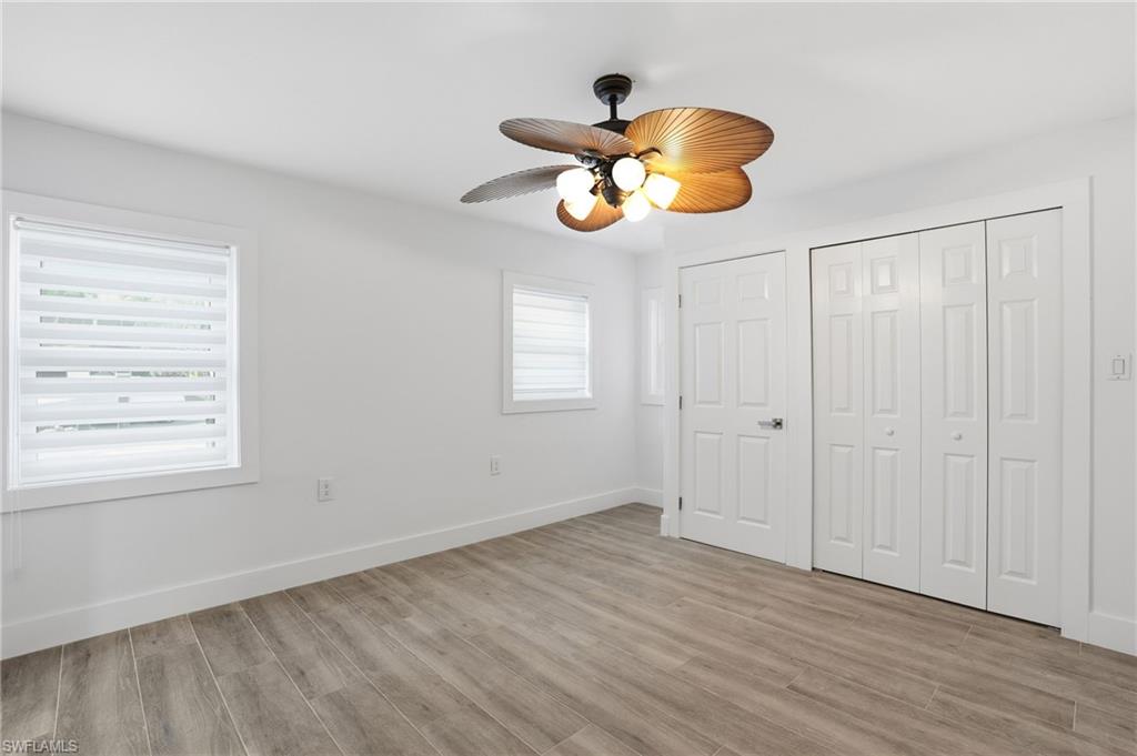 Unfurnished bedroom featuring light wood-style flooring, multiple windows, a ceiling fan, and a closet - Virtually Edited Image