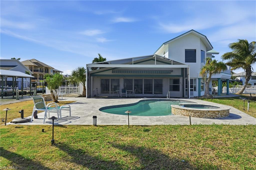 Back of property featuring a patio, a sunroom, a pool with connected hot tub, and stucco siding - Virtually Edited Image
