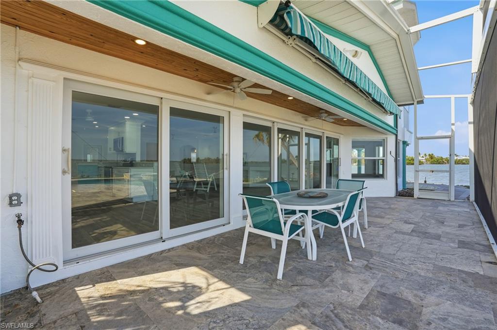 View of patio with a sunroom, a water view, glass enclosure, a ceiling fan, and outdoor dining area - Virtually Edited Image