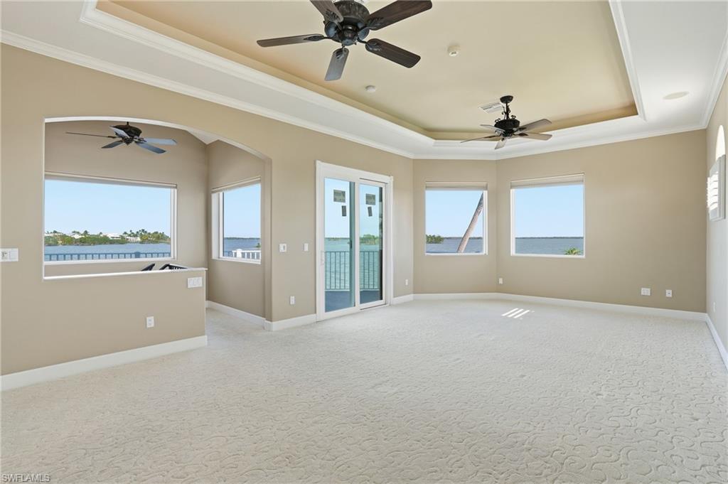 Unfurnished room with ceiling fan, ornamental molding, a tray ceiling, a water view, and plenty of natural light - Virtually Edited Image