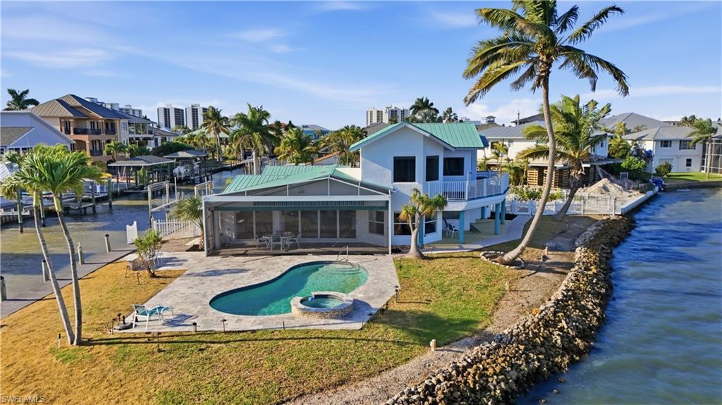 Back of house with a sunroom, a water view, a metal roof, and a patio area - Virtually Edited Image