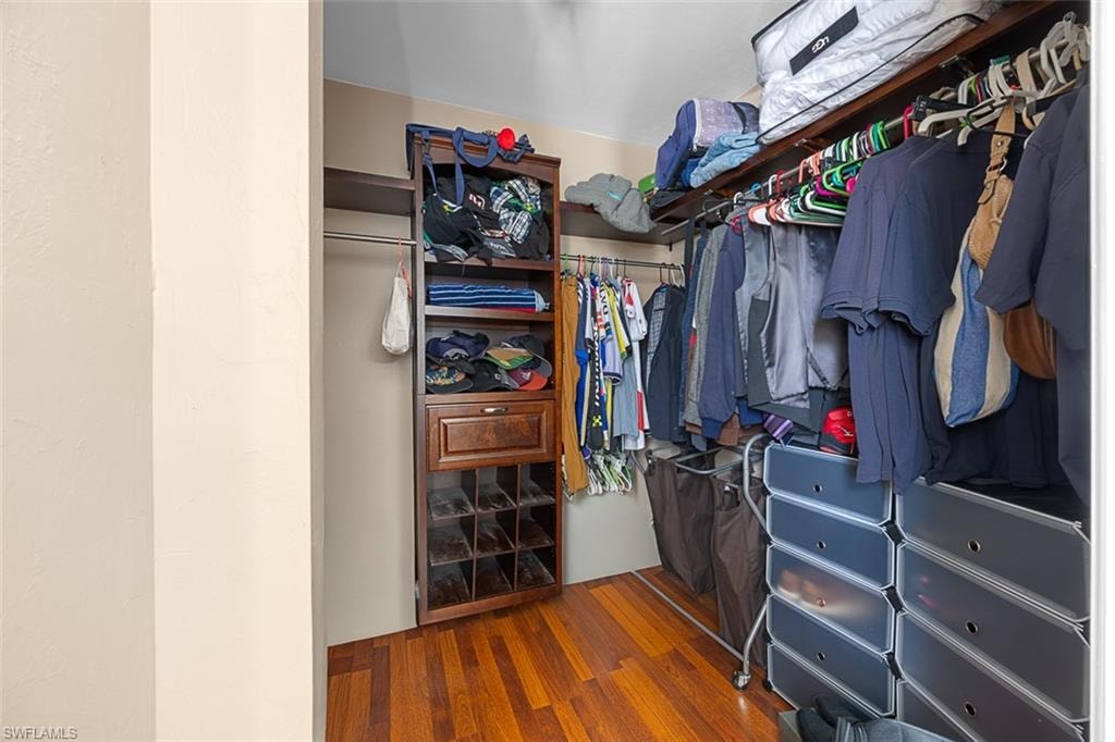 Custom closet system featuring wood-finish flooring, multiple hanging rods, built-in shelving, a shoe rack, and integrated drawers
