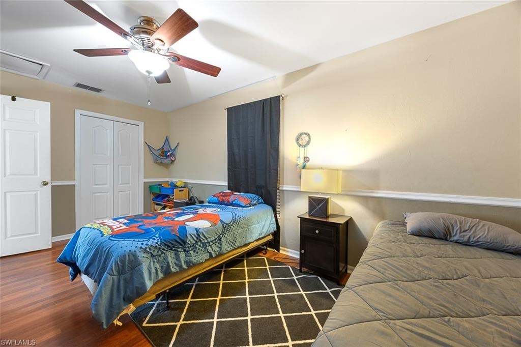 Bedroom featuring wood-finish flooring, two-tone painted walls with chair rail molding, and a ceiling fan with integrated lighting