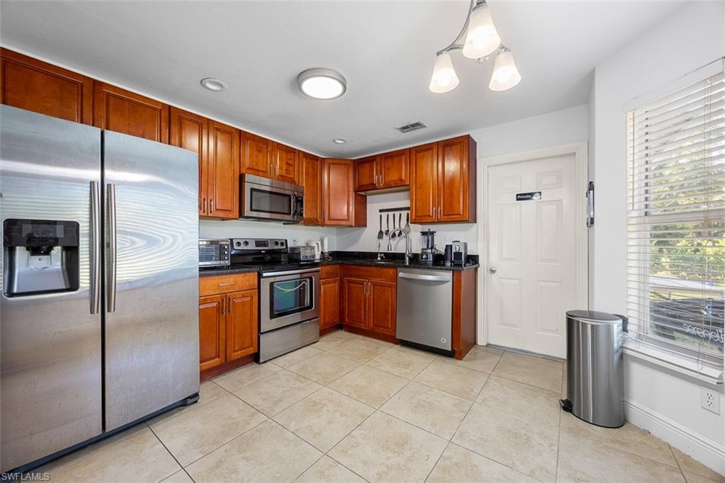 Kitchen featuring wood cabinetry, stainless steel appliances, dark countertops, and tile flooring