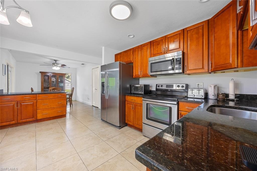 Kitchen featuring wood cabinetry, stainless steel appliances, dark granite-look countertops, and tile flooring