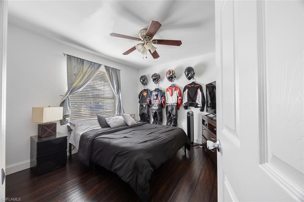 Bedroom featuring wood-finish flooring, a ceiling fan with integrated lighting, and a window with blinds and drapes
