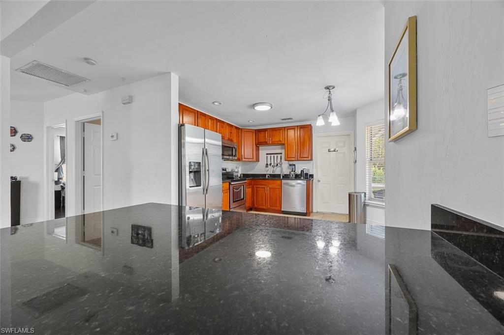 Kitchen featuring dark granite countertops, wood cabinetry, and stainless steel appliances including a refrigerator, dishwasher, and range with microwave