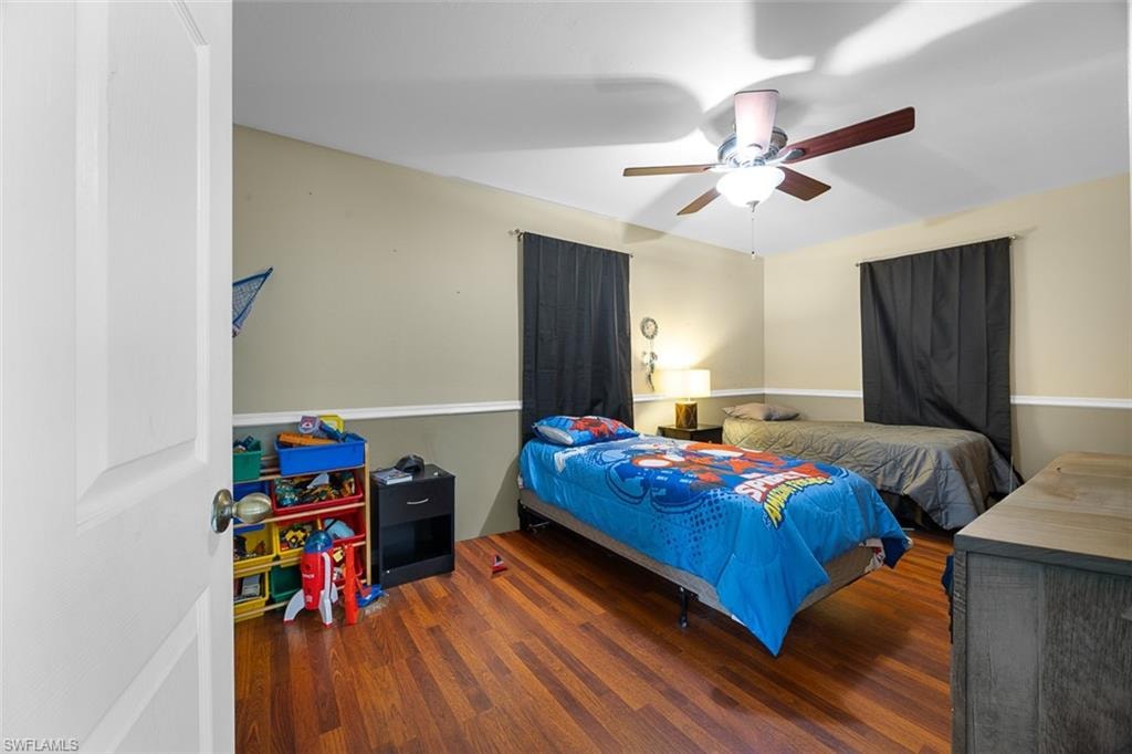 Spacious room featuring rich wood-finish flooring, a ceiling fan with light fixture, and neutral wall tones with white trim