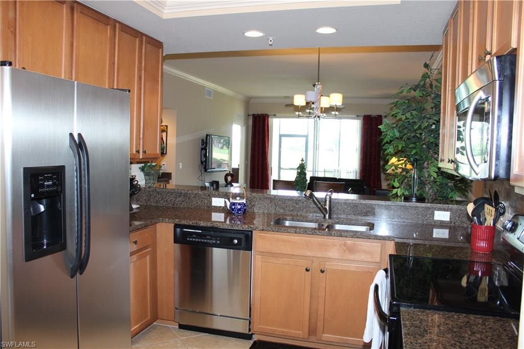 Kitchen with appliances with stainless steel finishes, ornamental molding, brown cabinetry, dark stone countertops, and decorative light fixtures