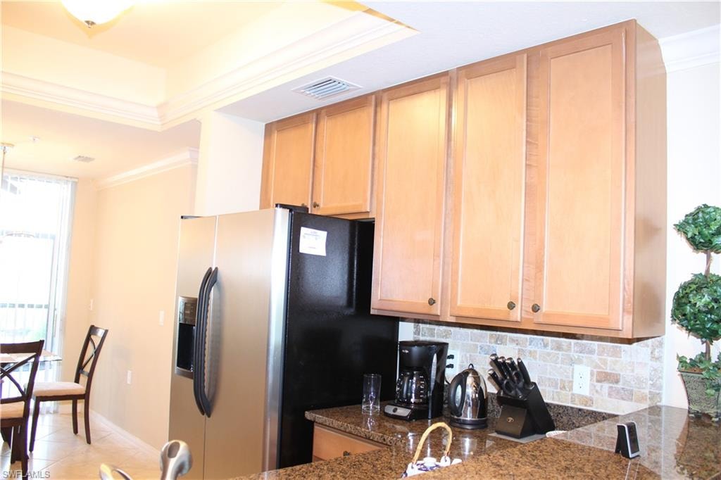 Kitchen with crown molding, backsplash, stainless steel refrigerator with ice dispenser, decorative light fixtures, and light tile patterned floors