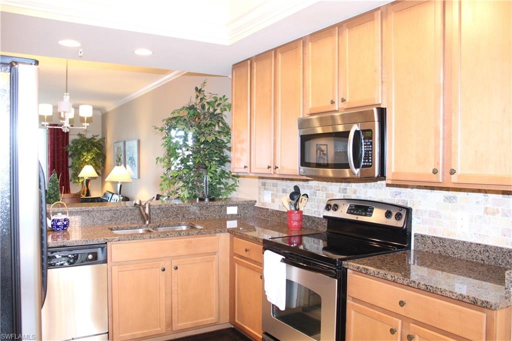 Kitchen with stainless steel appliances, crown molding, dark stone countertops, tasteful backsplash, and light brown cabinetry