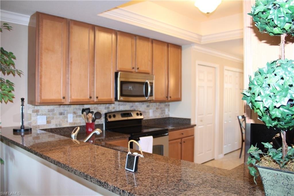 Kitchen with stainless steel appliances, ornamental molding, backsplash, dark stone countertops, and brown cabinets