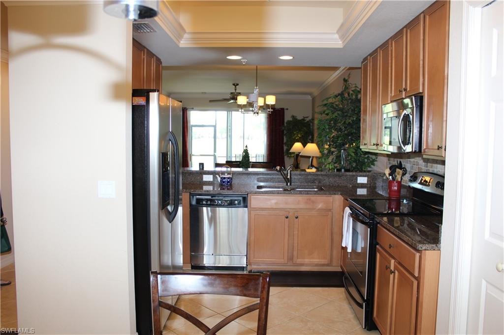 Kitchen featuring appliances with stainless steel finishes, dark stone counters, decorative backsplash, crown molding, and light tile patterned floors