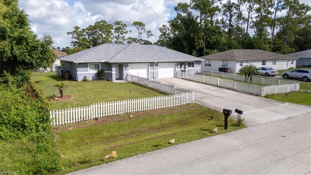 Duplex property featuring a light gray exterior, white picket fencing, and a dual concrete driveway