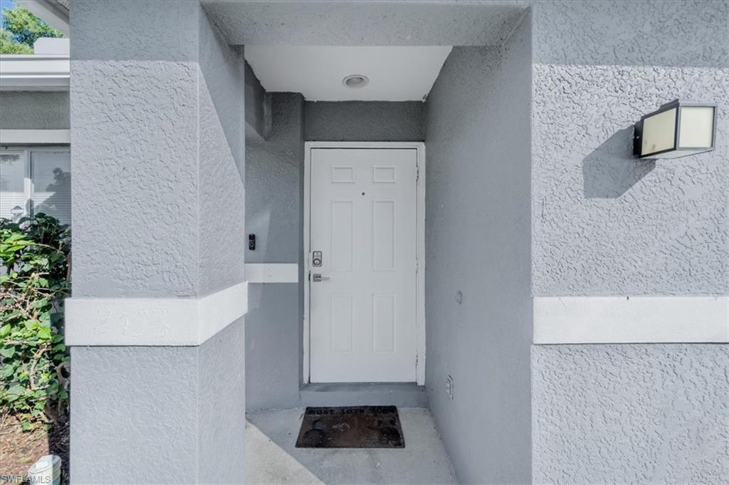 Entryway featuring a white door, textured exterior walls, an overhead recessed light, and an exterior wall-mounted light fixture