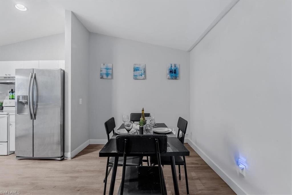 Vaulted ceiling dining area featuring wood-finish flooring, a contemporary black dining table, and a stainless steel side-by-side refrigerator