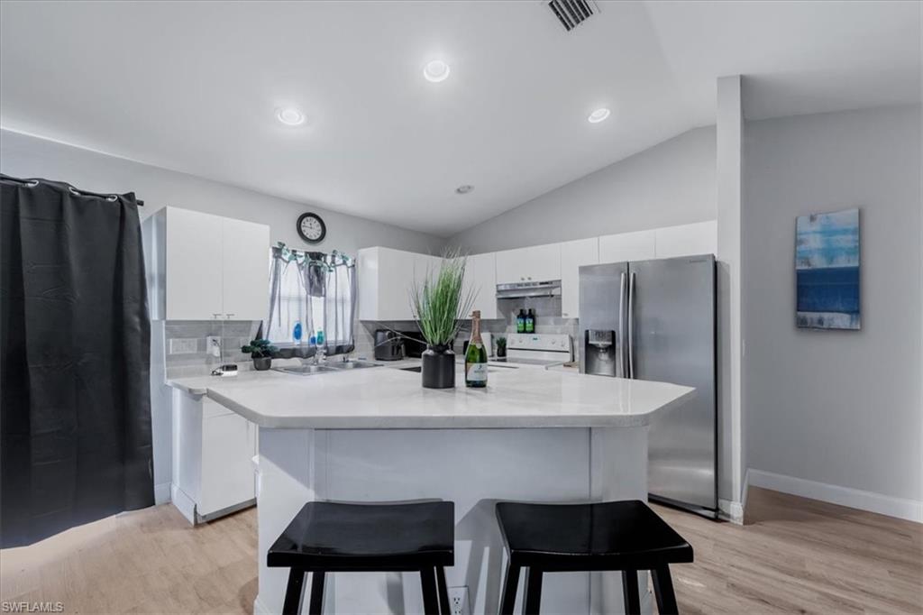 Kitchen featuring an island with stone countertop, white cabinetry, stainless steel refrigerator, white tile backsplash, and light wood-finish flooring