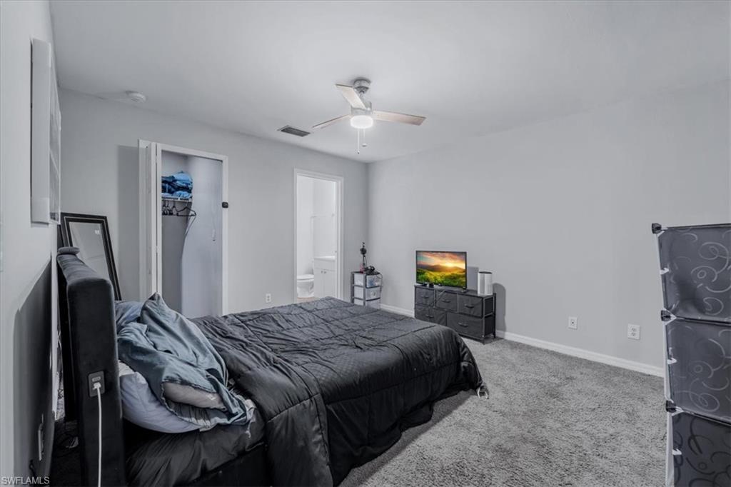 Carpeted room with a ceiling fan, closet, and a doorway revealing a partial bathroom with a toilet and vanity