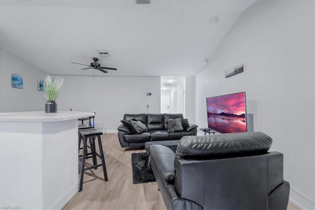Open concept living space featuring light wood-finish flooring, a contemporary ceiling fan, and a built-in breakfast bar with a light-toned countertop
