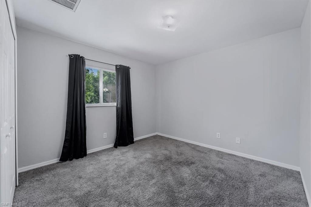 Carpeted room featuring light gray walls, a window with exterior tree views, and white baseboards