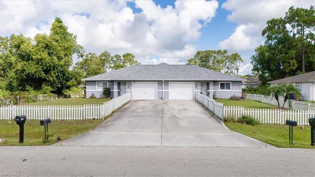 Duplex property featuring a light gray exterior, white picket fence, and a shared concrete driveway