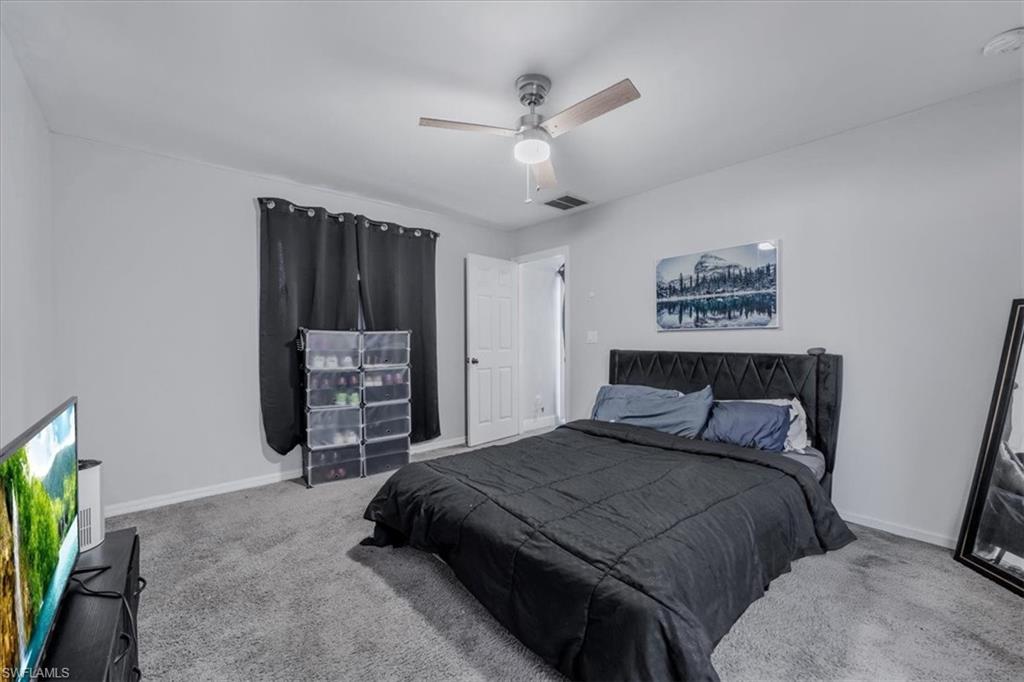 Bedroom featuring textured gray carpeting, neutral wall paint, and a ceiling fan with light fixture