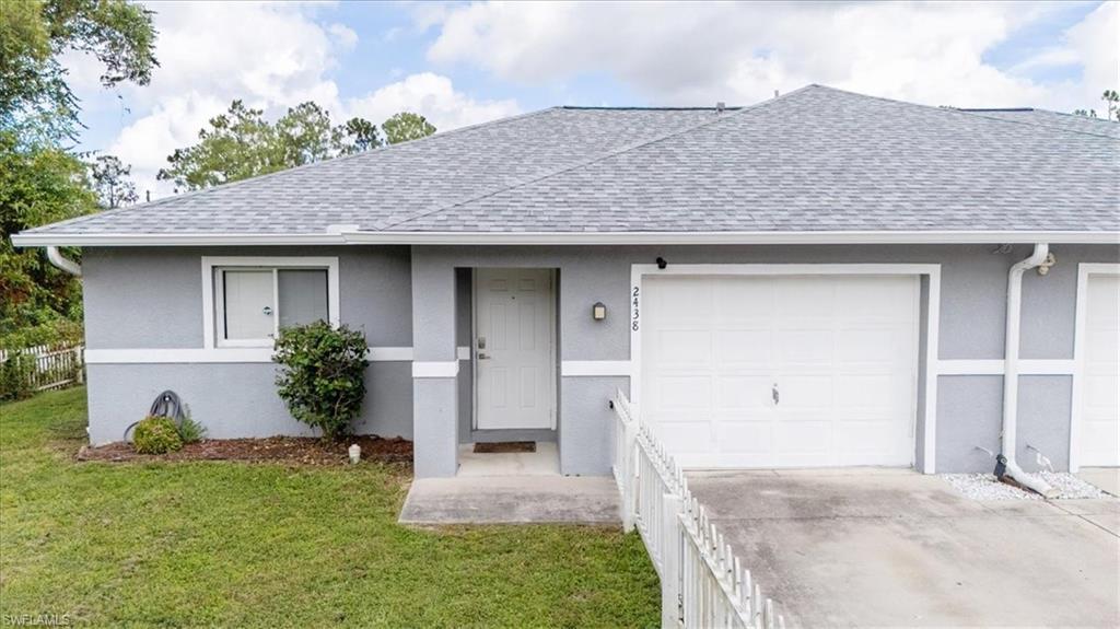 Gray exterior featuring a white entry door, an attached garage, a new shingle roof, and a front yard with mature landscaping