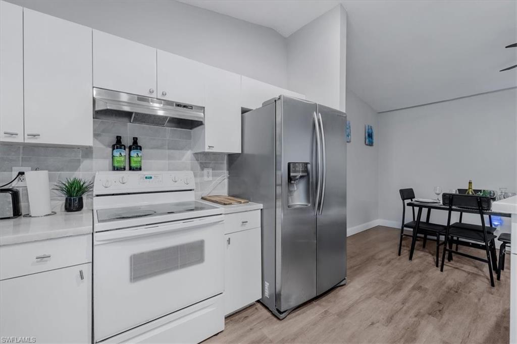 Contemporary kitchen featuring white cabinetry, light countertops, a white electric range with an overhead stainless steel exhaust hood, a subway tile backsplash, and wood-finish flooring