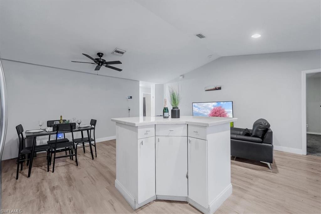 Open-concept living area featuring wood-finish flooring, a contemporary ceiling fan, and a built-in kitchen island with a light-toned countertop and white cabinetry