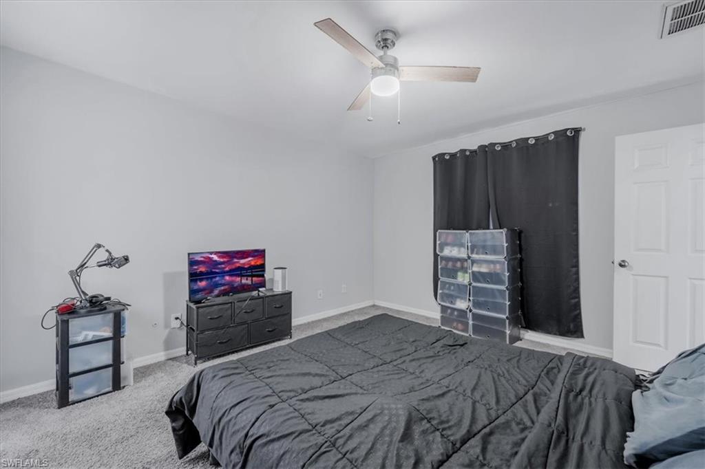 Interior room featuring light gray walls, gray carpeting, a ceiling fan with light fixture, a window with dark curtains, and a white interior door with a silver knob