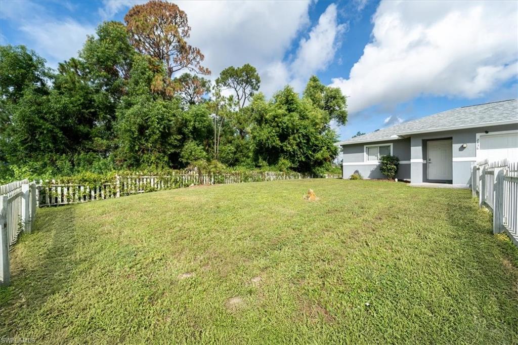 Expansive grassy yard with a white picket fence bordering mature trees
