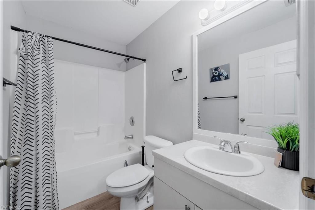 Full bathroom featuring a white tub/shower combination, wood-finish flooring, and a white vanity with an integrated sink
